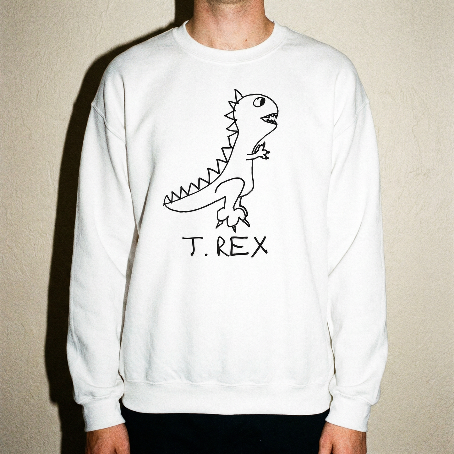 Model in a T-Rex sweatshirt against a stark beige backdrop, arms slightly out, committed