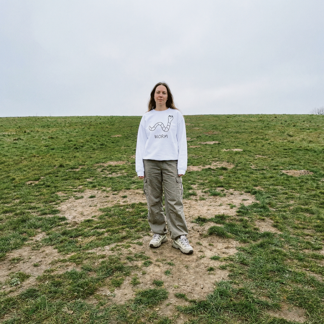 Person wearing a white sweatshirt with a lofi worm design and text, standing in a grassy field.